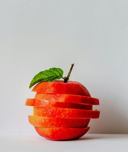 Kreativ angeordneter Apfel in Scheiben geschnitten mit einem Minzblatt oben auf weißem Hintergrund