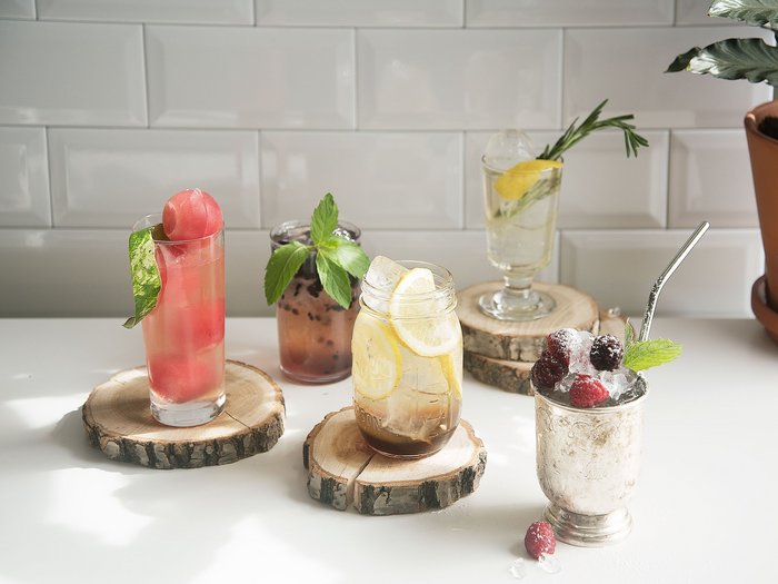 Auswahl verschiedener Cocktails ohne Alkohol, dekoriert mit verschiedenem Obst und Kräutern, serviert auf Holzuntersetzern  
