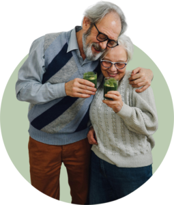 Ein lächelndes älteres Paar, das sich herzlich im Arm hält und gemeinsam grüne Smoothies in Gläsern hält
