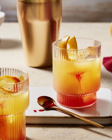 Zwei Orange Sour Cocktails mit eindrucksvollem Farbverlauf von Orange zu Rot, garniert mit Orangenscheiben, präsentiert auf einer modernen Marmorplatte