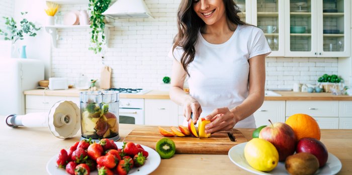 Lächelnde Frau bereitet in ihrer Küche einen frischen Obstsalat zu, eine gesunde Alternative zu kalorienreichen alkoholischen Getränken