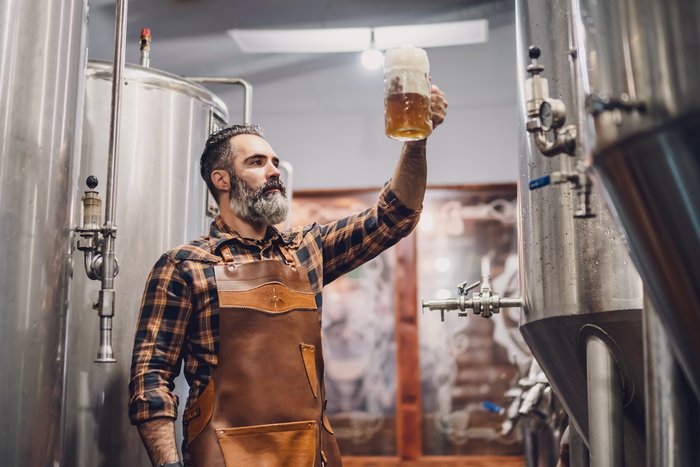 Braumeister prüft die Qualität von alkoholfreiem Bier im Brauereitank, veranschaulicht den Prozess der Herstellung alkoholfreier Getränke auf einer Informationsseite.
