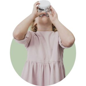 Ein kleines Mädchen in einem rosafarbenen Kleid hält eine große Tasse mit beiden Händen an ihren Mund und trinkt mit dem Kopf im Nacken