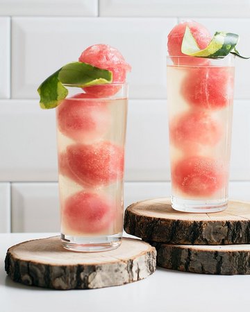 Erfrischende Wassermelonen-Ingwer-Mocktails mit gefrorenen Wassermelonenkugeln und einem Hauch von Ingwer, dekoriert mit Limettenschalen auf rustikalen Holzscheiben